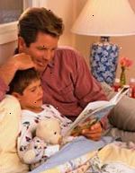 Immagine di padre ascoltando il figlio leggere un libro prima di coricarsi
